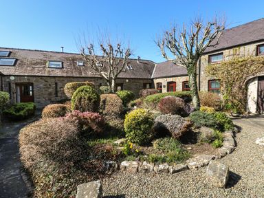 A stone cottage courtyard with pruned trees and various shrubs at Corner Cottage in Broad Haven