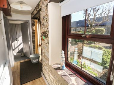 A hallway with a window showing a garden and a grey boot bin on the floor at Corner Cottage in Broad Haven