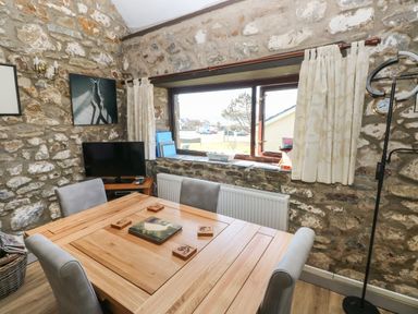 A dining area with a wooden table and gray chairs near a window in a stone wall room at Corner Cottage in Broad Haven