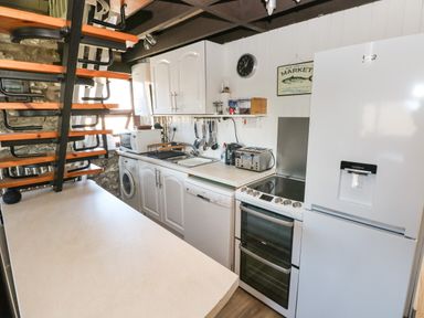 A kitchen with white cabinets appliances and a staircase at Corner Cottage in Broad Haven