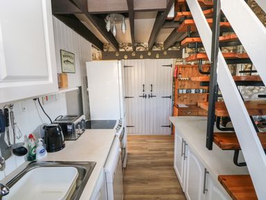 A kitchen with white cabinets wooden stairs and a wooden cabinet at Corner Cottage in Broad Haven