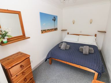 A bedroom with a wooden bed with blue striped bedding and a wooden chest of drawers at Corner Cottage in Broad Haven