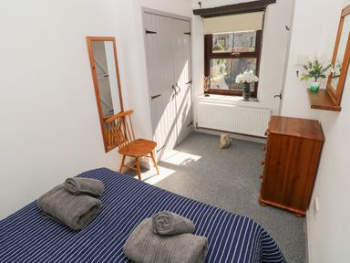 A bedroom with a bed striped bedding wooden chair wall mirror dresser and window at Corner Cottage in Broad Haven