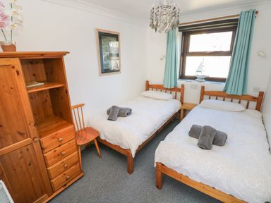 A bedroom with two single beds wooden furniture and a window with curtains at Corner Cottage in Broad Haven