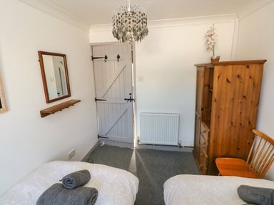A bedroom with two beds with towels a wooden wardrobe a wooden chair a wall mirror and a door at Corner Cottage in Broad Haven