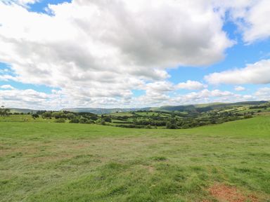 A grassy field with trees and hills under a partly cloudy sky at Valley View in Rhayader