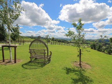 A garden with grass and trees with a wooden bench and a rural landscape at Valley View in Rhayader