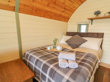 A bedroom with a double bed covered by a checkered blanket and towels on top at Valley View in Rhayader