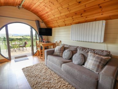 A living area with a sofa a dining table and chairs a television and large round doors opening to a patio at Valley View in Rhayader