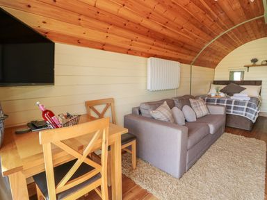 A small wooden interior with a dining table and chairs a gray sofa and a bed at Valley View in Rhayader