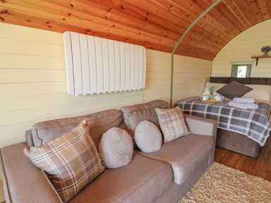 An interior room with a beige sofa with cushions and a bed with a checked blanket at Valley View in Rhayader