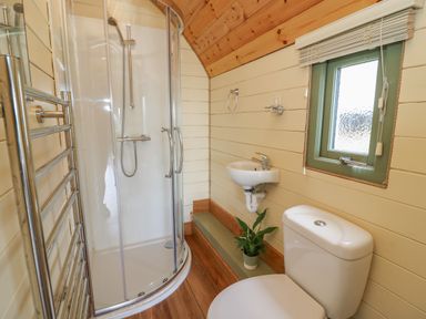 A bathroom with a curved glass shower enclosure a white toilet a small wall-mounted sink a window and a towel rack at Valley View in Rhayader