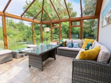 A conservatory with seating and outdoor views at Dragonfly Lodge Whinburgh near Dereham