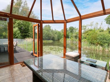 A conservatory with a glass table and view of water at Dragonfly Lodge Whinburgh near Dereham