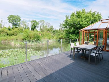 An outdoor seating area overlooking a pond at Dragonfly Lodge in Whinburgh near Dereham