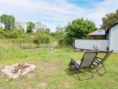A garden with chairs and a fire pit near a pond at Dragonfly Lodge in Whinburgh near Dereham