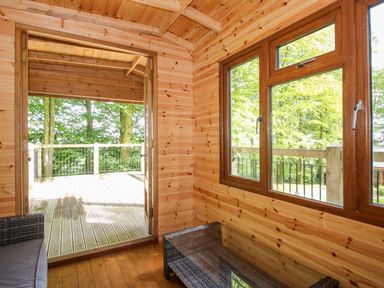 A snug with wooden walls and windows leading to an outdoor deck at Valley View Lodge in Welshpool
