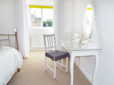 A bedroom corner with a white dressing table and chair near a window at Kates Cottage in Bourton-on-the-Water