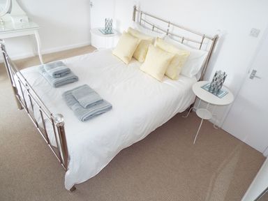 A bedroom with a metal bed frame white bedding yellow pillows gray towels on the bed and two white bedside tables at Kates Cottage in Bourton-on-the-Water