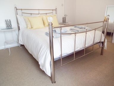 A bedroom with a metal framed bed with white bedding and yellow pillows and side tables at Kates Cottage in Bourton-on-the-Water
