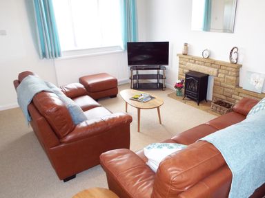 A living room with two brown leather sofas a small wooden coffee table a television on a stand and a fireplace at Kates Cottage in Bourton-on-the-Water
