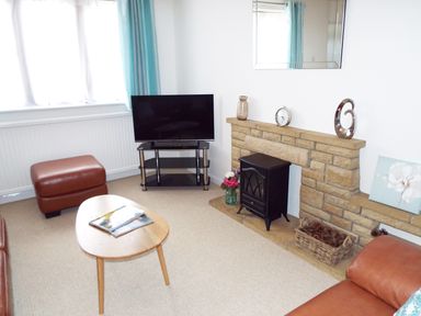 A living room with a television on a stand a leather ottoman a wooden coffee table and a stone fireplace at Kates Cottage in Bourton on the Water