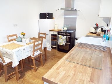 A kitchen with wooden chairs around a table a stove refrigerator and a sink at Kates Cottage in Bourton-on-the-Water