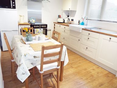 A kitchen with wooden dining table and chairs white cabinets stove and sink at Kates Cottage in Bourton-on-the-Water