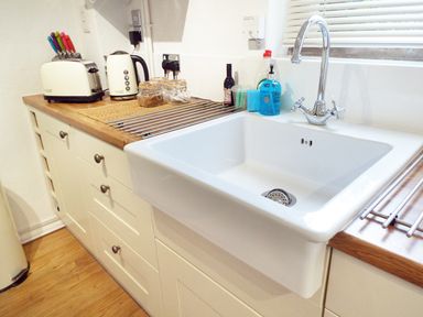A kitchen sink with a faucet on a wooden countertop with jars a kettle and a toaster at Kates Cottage in Bourton-on-the-Water