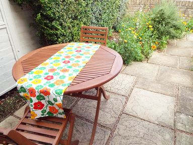 A wooden table with two chairs on a stone patio next to a garden with flowers at Kates Cottage in Bourton-on-the-Water
