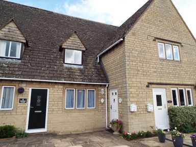 The exterior of a stone cottage with three doors and several windows at Kates Cottage in Bourton-on-the-Water