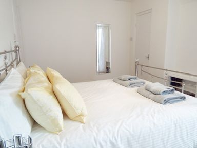 A bedroom with a metal bed frame yellow pillows white bedding gray towels and a wall mirror at Kates Cottage in Bourton-on-the-Water