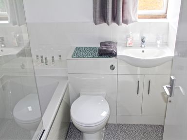 A bathroom with a toilet sink countertop with towel and toiletries and a bathtub with glass panel at Kates Cottage in Bourton-on-the-Water