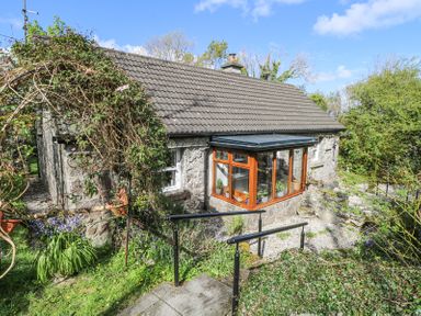 A stone cottage with a glass sunroom and tiled roof surrounded by greenery and flowers at Dun na Ron in Oughterard County Galway