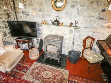 A room with a fireplace stove television armchair and wooden chair at Dun na Ron in Oughterard County Galway