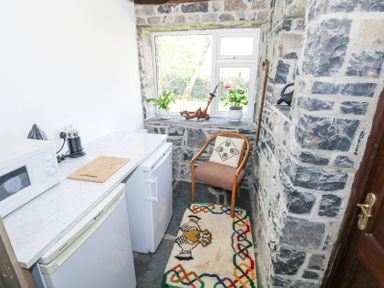 A small kitchen area with a microwave and coffee maker on a marble countertop two refrigerators a wooden chair with a cushion a colorful rug and a window with plants on the sill at Dun na Ron Oughterard County Galway