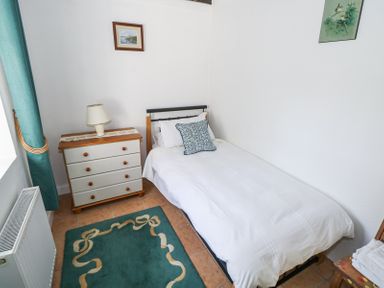 A small bedroom with a single bed a chest of drawers with a lamp a teal rug and framed pictures on the wall at Dun na Ron in Oughterard County Galway