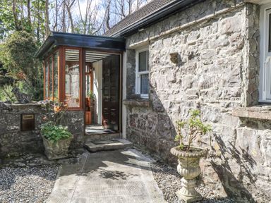 Exterior view of a stone wall house with a glass enclosed porch and two plant pots outside at Dun na Ron in Oughterard County Galway