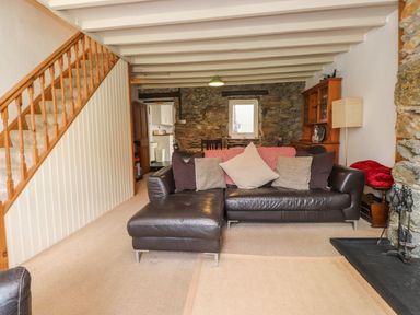 A living room with a leather sofa stair railing stone wall and a small window at Nantmel in Beddgelert