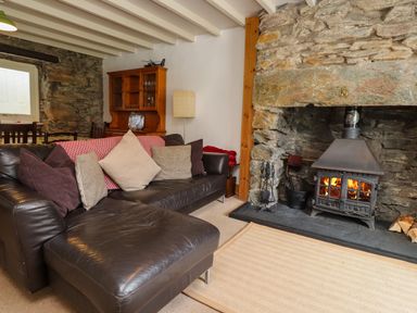 A living room with a leather sofa and cushions beside a stone fireplace with a wood burning stove at Nantmel in Beddgelert