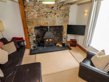 A living room with a stone fireplace wood burning stove two leather sofas a television on a stand and a window with curtains at Nantmel in Beddgelert