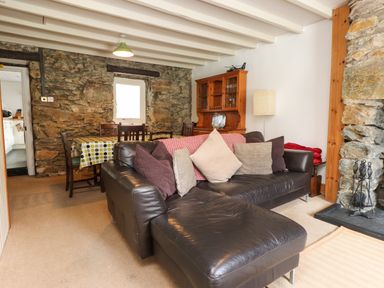 A living room with a black leather sofa and dining table with chairs near a stone wall at Nantmel in Beddgelert