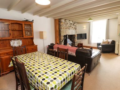 A dining table with a polka dot tablecloth and wooden chairs next to a wooden cabinet and living room with sofas fireplace and television at Nantmel in Beddgelert