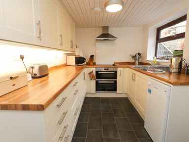 A kitchen with wooden countertops white cabinets an oven microwave toaster dish rack and kettle at Nantmel in Beddgelert
