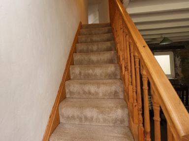 A carpeted staircase with wooden railing and white wall at Nantmel in Beddgelert
