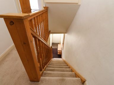 A carpeted staircase with wooden banister leading down to a hallway with a bench at Nantmel in Beddgelert