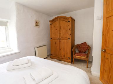 A bedroom with a bed with towels a wooden wardrobe a wicker chair and a window at Nantmel in Beddgelert