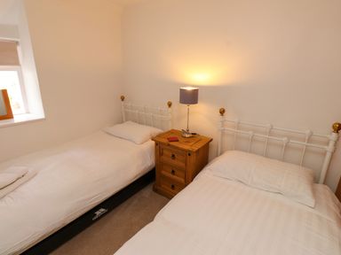 A bedroom with two single beds a wooden nightstand and a lamp at Nantmel in Beddgelert