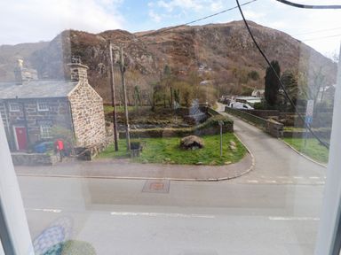 A stone house with a red door near a grassy area and a narrow road with a stone bridge and hills in the background at Nantmel in Beddgelert