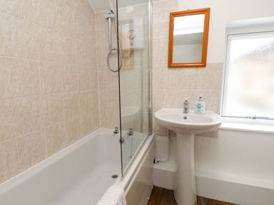 A bathroom with a bathtub shower combination a pedestal sink a wooden framed mirror and a frosted window at Nantmel in Beddgelert